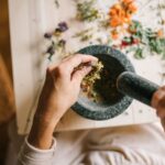 Top view of hands grinding dried herbs using a mortar and pestle on a wooden table.