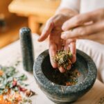 A woman uses a mortar and pestle to crush dried herbs for traditional medicine preparation.
